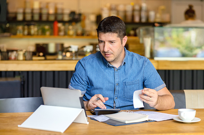 Empresario con calculadora y facturas mientras mira en laptop finanzas de su negocio